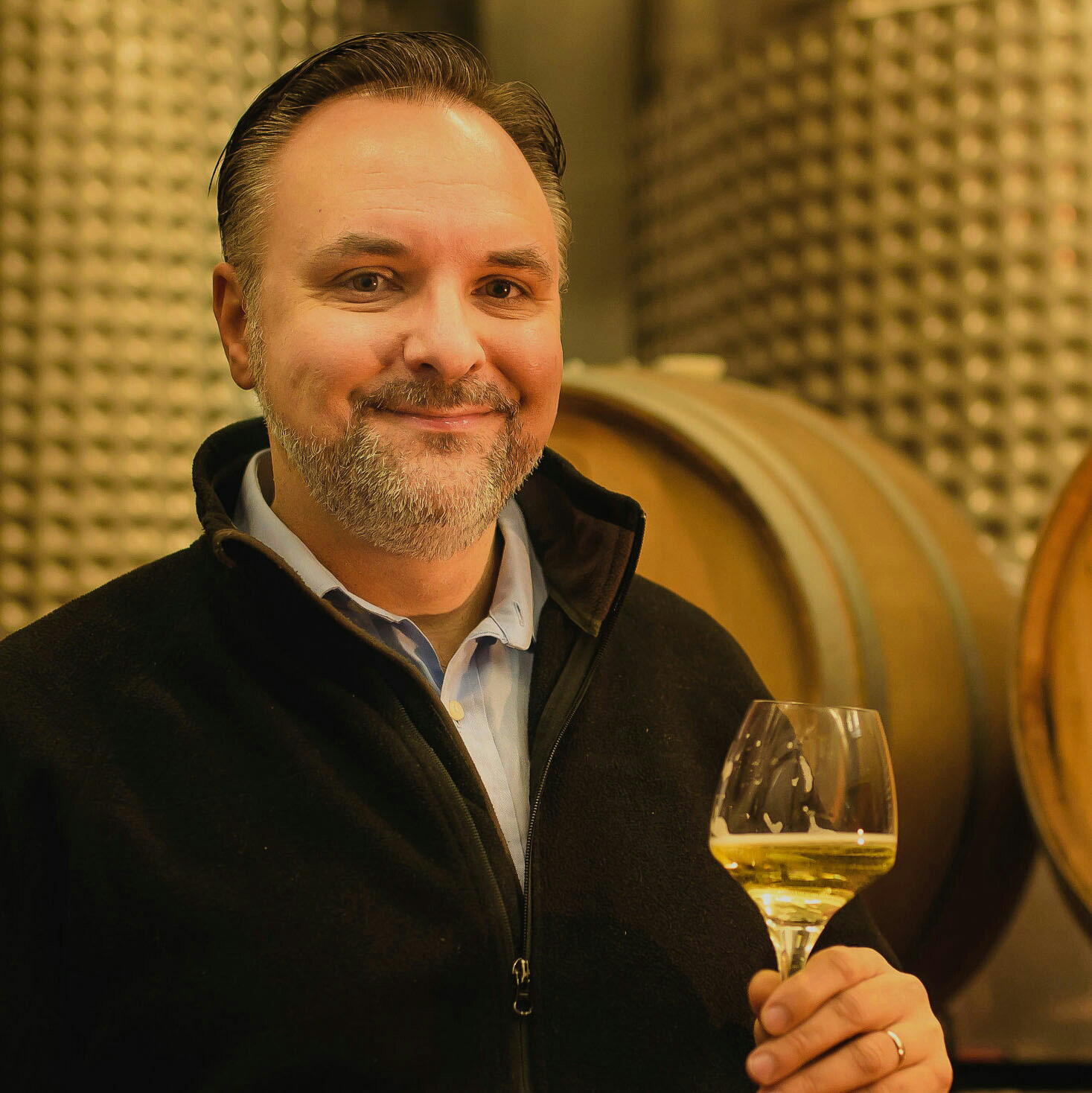 Dominic Rivard — winemaker and cider maker, holding a glass of white wine in a barrel cellar